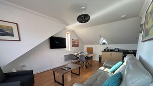 Eine moderne Wohnung mit Essbereich, einer Couch, einem Fernseher und einer Küche.