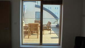 Ein Zimmer mit großem Fenster und Blick auf eine Terrasse mit Holzmöbeln.
