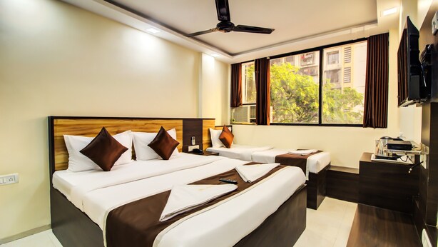 A hotel room with a large bed, a smaller bed, a desk, and a TV. - OPAL COMFORTS- A BUSINESS HOTEL (Navi Mumbai)