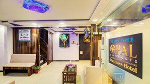 A hotel reception area with a sofa, a small table with a plant, and a sign welcoming guests to the hotel. - OPAL COMFORTS- A BUSINESS HOTEL (Navi Mumbai)