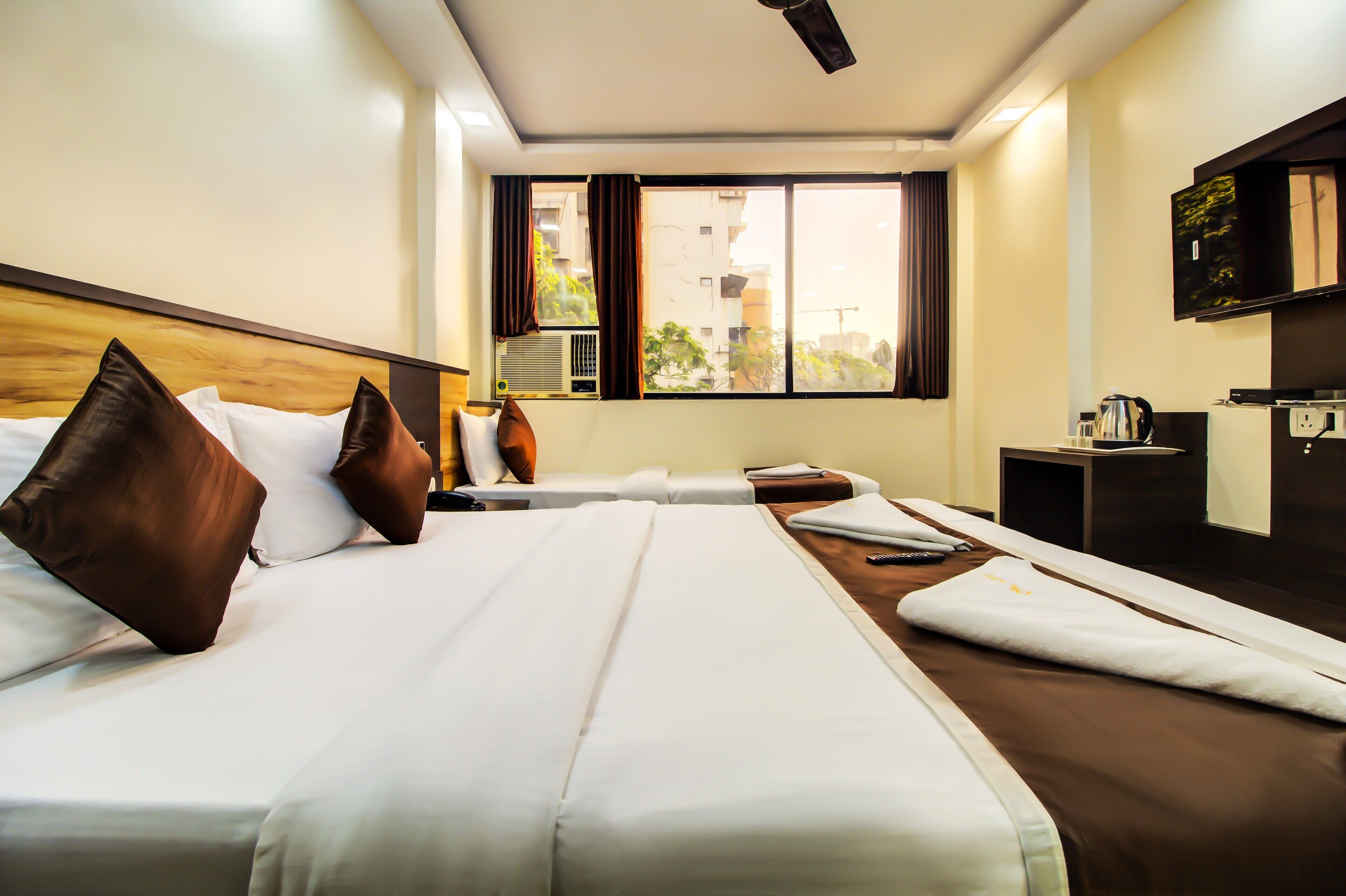 A hotel room with a large bed, a desk, a chair, a TV, and a window with curtains.