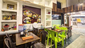 A restaurant with multiple tables and chairs, a wall with food images, and shelves with various items. - OPAL COMFORTS- A BUSINESS HOTEL (Navi Mumbai)