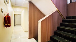 A staircase with wooden steps and a handrail, leading to a landing. A fire extinguisher is mounted on the wall to the left. - OPAL COMFORTS- A BUSINESS HOTEL (Navi Mumbai)