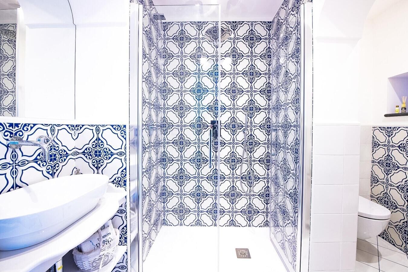 Een badkamer met een douchegedeelte, betegeld met blauw-witte patronen, een wit wastafelmeubel en een toilet.