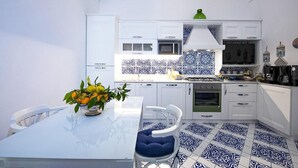 A modern kitchen with white cabinets, a blue and white patterned backsplash, and a dining area with a glass table and blue cushioned chairs.