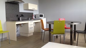A modern kitchen with a microwave, stove, and cabinets. There is a dining table with chairs and a small round table with a chair. - Résidence Apparten Ville Appartement 6 Personnes (Saint-Flour)