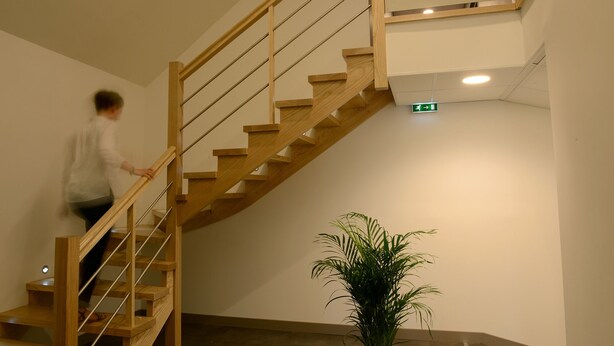 A wooden staircase with a handrail, a sign reading "Résidence Apart' en Ville", and a green emergency exit sign. - Résidence Apparten Ville Appartement 6 Personnes (Saint-Flour)