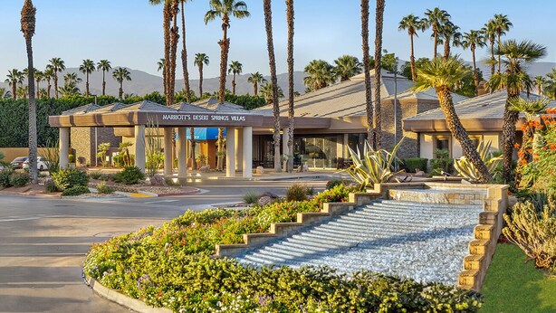 A hotel with a desert-themed exterior, palm trees, and a landscaped garden.