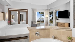 A hotel room with a large bed, a bathtub, a TV, and a view of the outdoors.