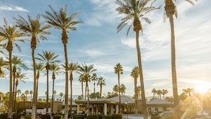 A hotel with a central building surrounded by palm trees and a grassy area.