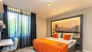 Quarto de hotel moderno com uma cama grande, uma escrivaninha e vista para a cidade pela janela.