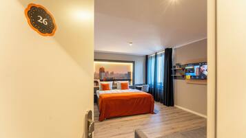 Una habitación de hotel con una cama, vistas a la ciudad, un televisor y una puerta con un número.