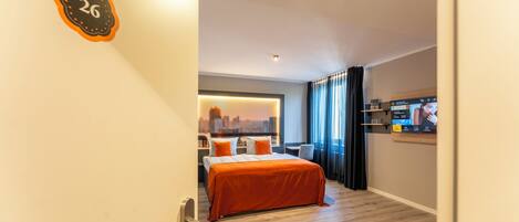 A hotel room with a bed, a cityscape view, a TV, and a door with a number.