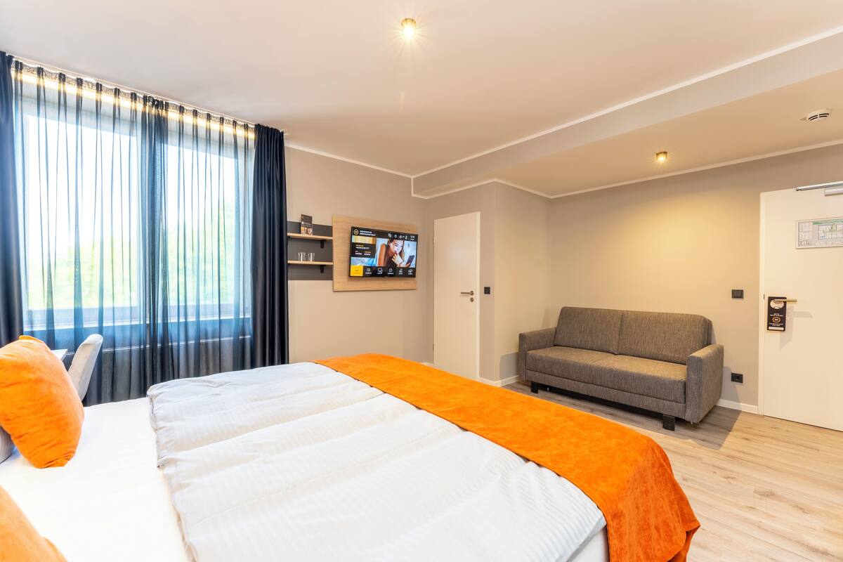 A hotel room with a bed, a sofa, a TV, and a door.