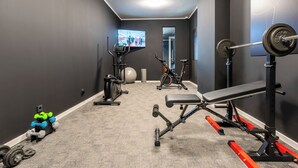Uma academia em casa com equipamentos de ginástica, uma TV e um espelho.