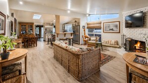 A spacious living area with a large wicker sofa, a fireplace, and a kitchen in the background.