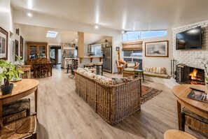 A spacious living area with a large wicker sofa, a fireplace, and a kitchen in the background.