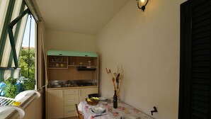 Une cuisine compacte avec un coin repas, une fenêtre avec des rideaux et un luminaire fixé au mur.