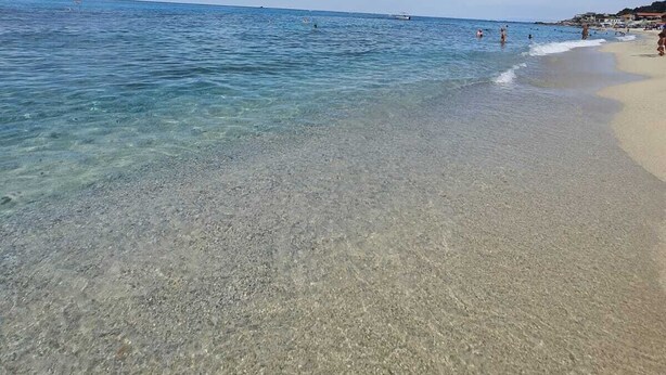 Une plage avec une eau claire et peu profonde, un rivage sablonneux et quelques personnes au loin.