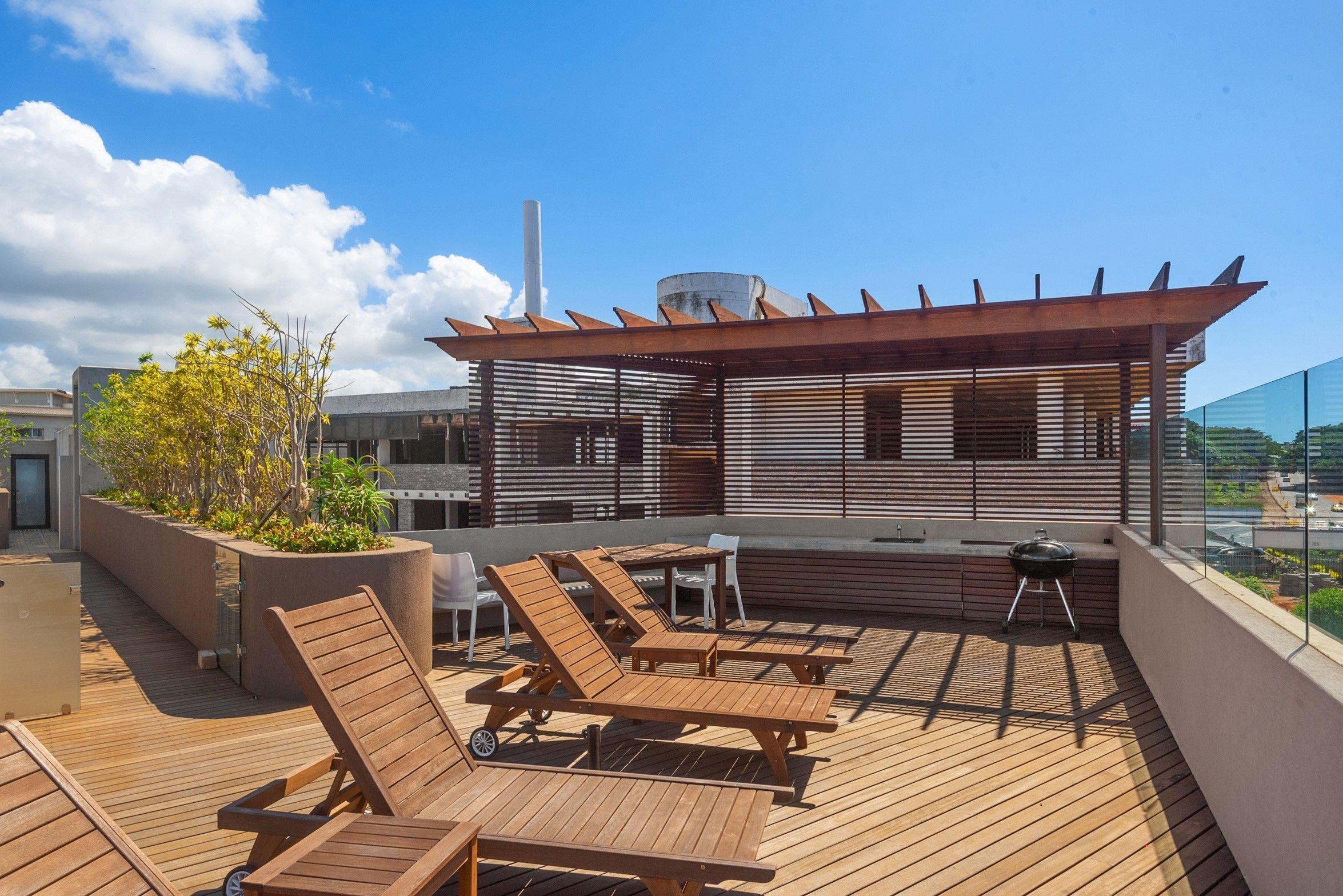 Une terrasse sur le toit, dotée de chaises longues en bois, d’un barbecue et d’une pergola.