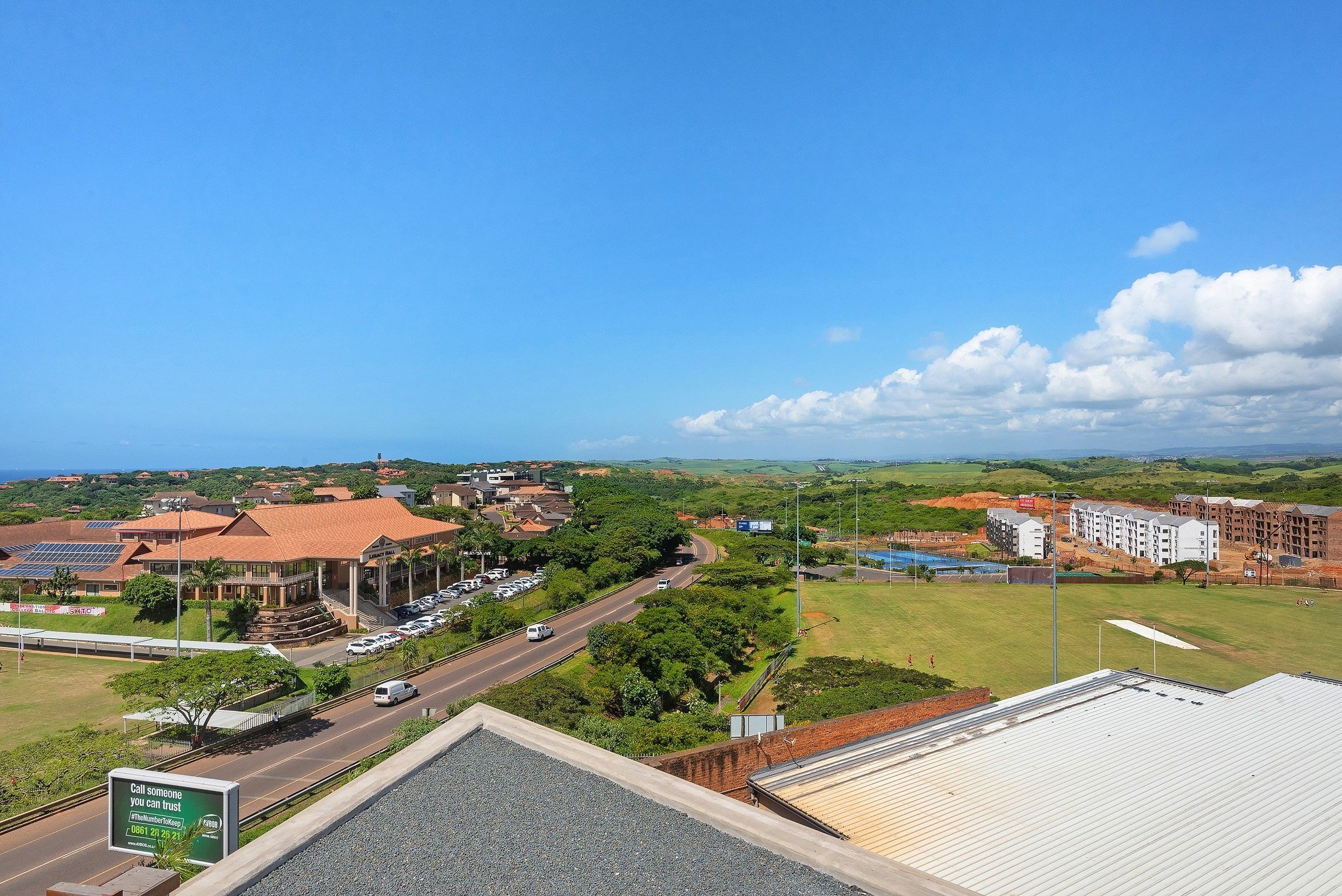 A view of a road with buildings and greenery in the background.