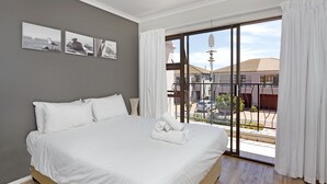 Ein Schlafzimmer mit einem großen Bett, weißer Bettwäsche und Blick durch eine Schiebetür nach draußen.