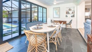 A dining area with a round table, wicker chairs, and a view of a swimming pool through large glass doors. - Welcome to your personal slice of paradise (Placida)