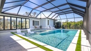 A modern house with a large glass-enclosed pool area, outdoor seating, and a view of the surrounding landscape. - Welcome to your personal slice of paradise (Placida)