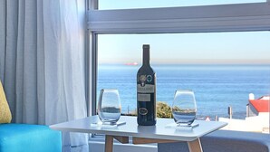 Quarto com uma mesa perto da janela com vista para o mar, apresentando uma garrafa de vinho e duas taças.