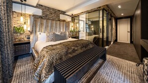 A modern bedroom with a stone accent wall, a large bed with a leopard print bedspread, a bench, and a glass-enclosed walk-in closet. - Aurum 101 - Two Bedroom Apartment, Sleeps 4 (Cape Town)