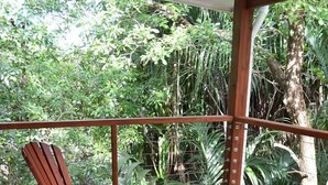 Une terrasse en bois avec deux fauteuils Adirondack et une petite table, le tout entouré d’une végétation tropicale luxuriante.