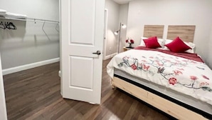Ein Schlafzimmer mit Holzboden, einem Bett mit floralem Bettzeug und roten Kissen, einer weißen Tür und einem Nachttisch mit Lampe.