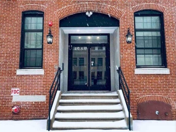 A brick building with a double door entrance, two windows on either side, and a staircase leading up to the door.