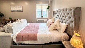 A bedroom with a large bed, a bedside table, a hanging plant, and a window with a view.