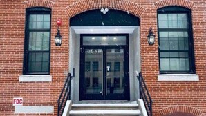 A brick building with a double door entrance, two windows on either side, and a fire hydrant on the left.