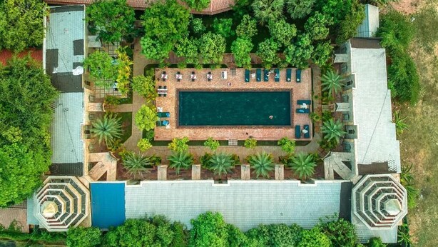 Vista aérea de un complejo turístico con una piscina central, rodeado de exuberante vegetación y palmeras.