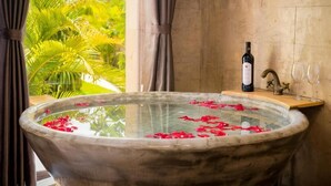 Una bañera llena de agua y pétalos de rosa, una botella de vino y un pequeño estante con copas sobre una encimera de madera.