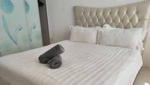 A neatly made bed with a striped bedspread and two rolled towels on it. - Simfoni Comfy 3BR Suite (Langkawi)