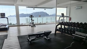 A gym with a treadmill, bench press, and dumbbells, overlooking a body of water and mountains. - Simfoni Comfy 3BR Suite (Langkawi)