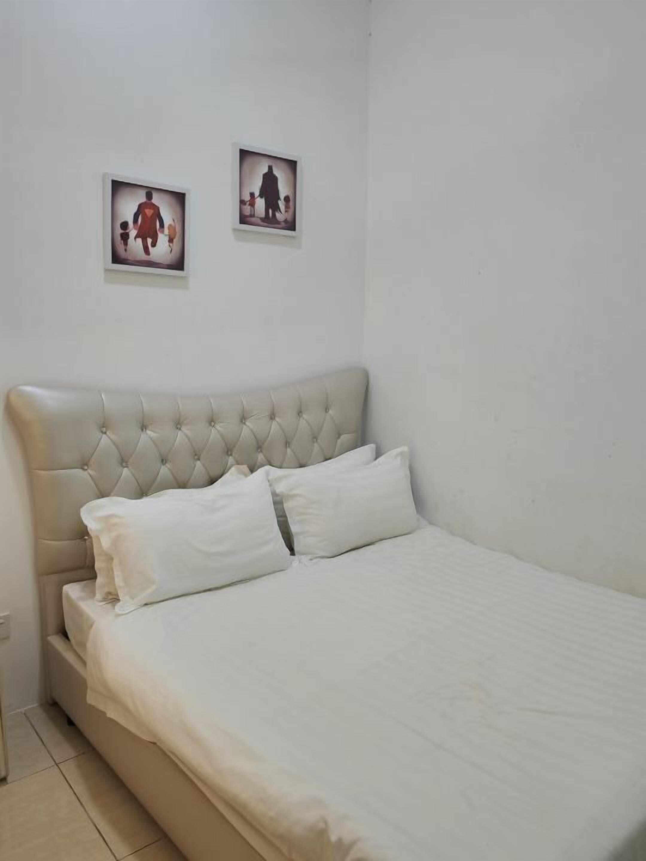 A bedroom with a tufted headboard, a bed with white linens, and two framed pictures on the wall.