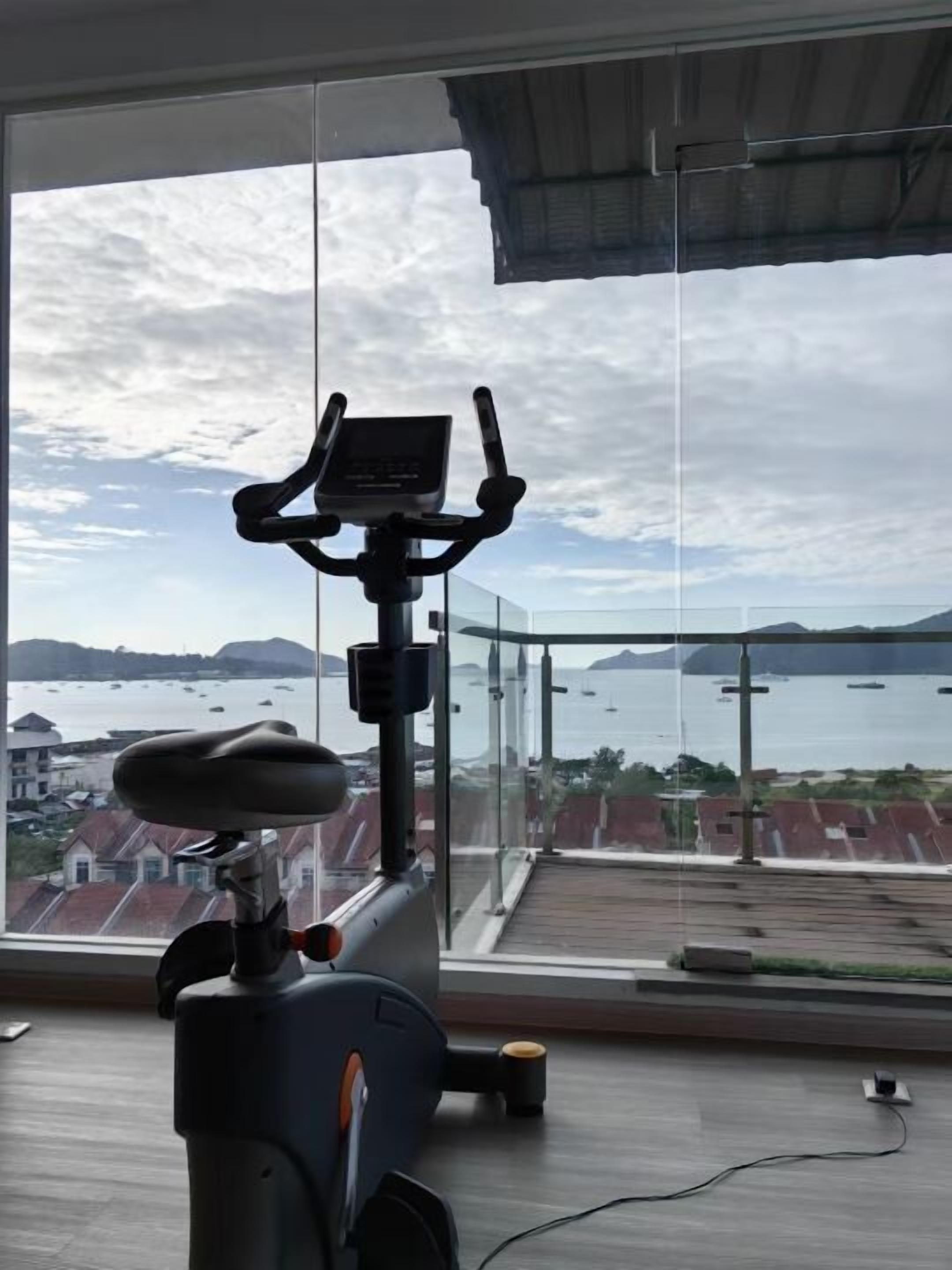 A stationary bike with a digital display, positioned in a room with a large window overlooking a coastal area with boats and buildings.