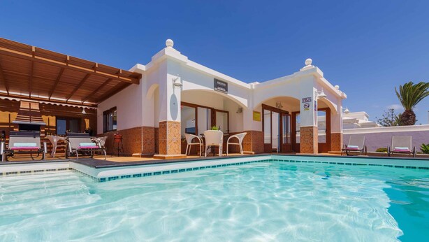 Un espace aménagé au bord de la piscine, avec des chaises longues, un coin salon couvert et un bâtiment sur lequel est apposée une enseigne indiquant « Superstar Beach Club ».