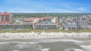 Een kuststadsgezicht met een hotel aan het strand, meerdere gebouwen en een strand met parasols.