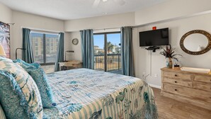 Een slaapkamer met een bed, een dressoir, een televisie en een balkon met gordijnen.