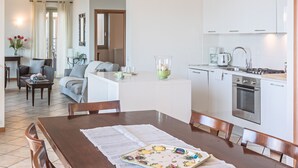 Une cuisine moderne avec des meubles blancs, un coin repas avec une table et des chaises en bois, et un salon avec un canapé et une table basse.