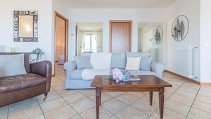 Un salon avec un canapé en cuir marron, un canapé gris agrémenté d’un plaid blanc et une table basse en bois sur laquelle est disposé un arrangement floral.