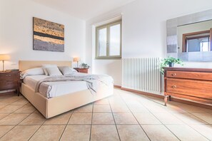 A bedroom with a bed, bedside tables, a dresser, a radiator, a window, and a painting on the wall. - Sunny Varenna Apartment (Perledo)