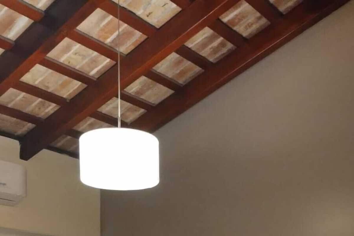 A hotel room with two beds, a wooden ceiling, a white lamp, and a wall-mounted air conditioner.