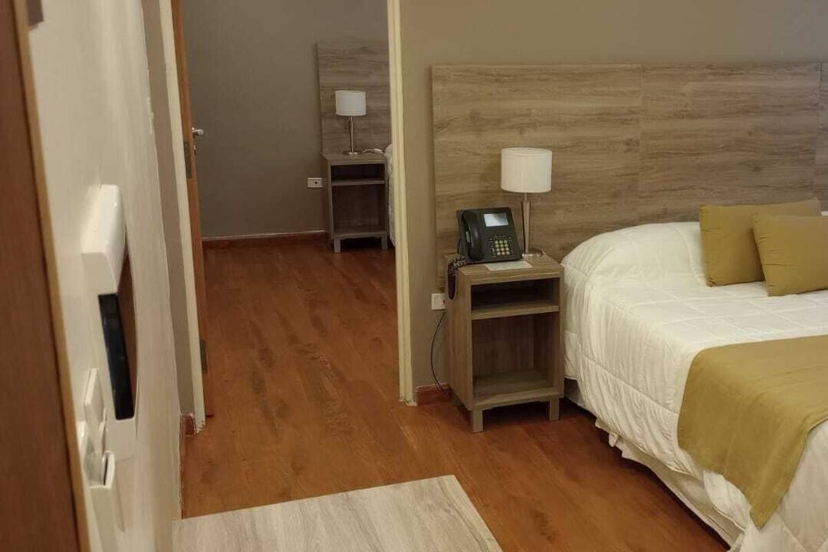 A hotel room with a wooden headboard, a bed with white bedding and two pillows, a bedside table with a lamp, and a telephone.