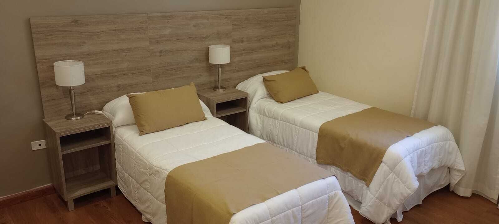 Two single beds with wooden headboards, bedside tables with lamps, and beige bedding.